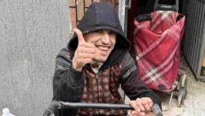 Mohsine sourit largement et fait un pouce levé, heureux après l’installation des batteries sur son fauteuil roulant électrique.