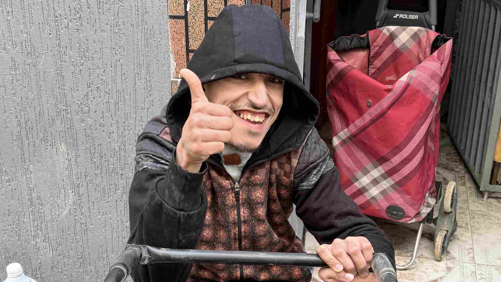 Accueil 5 Mohsine Sourit Largement Et Fait Un Pouce Levé, Heureux Après L’installation Des Batteries Sur Son Fauteuil Roulant Électrique.